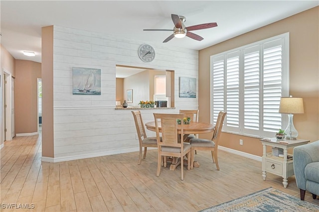 dining room featuring ceiling fan, light wood-type flooring, and wood walls