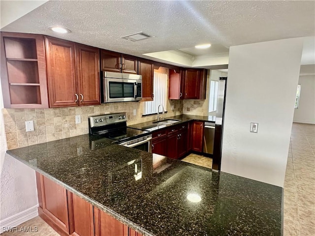 kitchen with appliances with stainless steel finishes, dark stone countertops, and kitchen peninsula