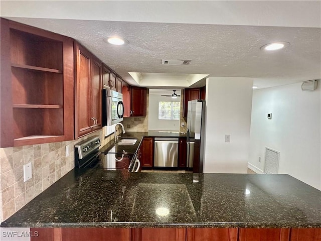 kitchen featuring appliances with stainless steel finishes, dark stone countertops, sink, backsplash, and kitchen peninsula