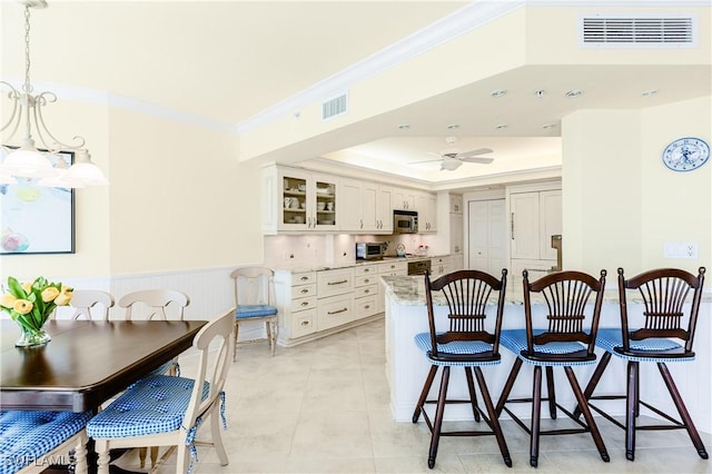 kitchen with crown molding, ceiling fan, white cabinetry, hanging light fixtures, and light stone countertops