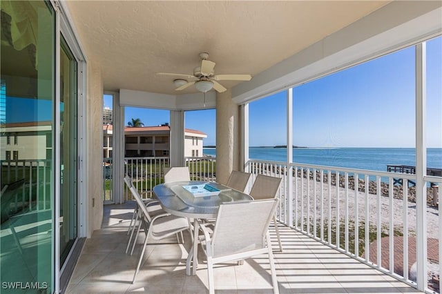 sunroom / solarium featuring ceiling fan, a beach view, and a water view