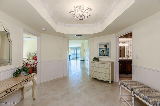 hallway featuring a tray ceiling, ornamental molding, and light tile patterned flooring