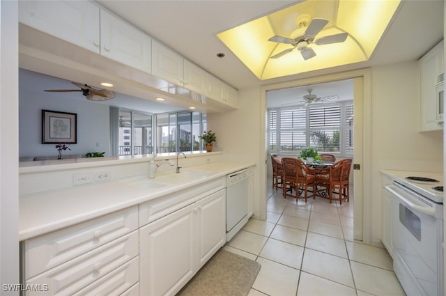 kitchen with a raised ceiling, white cabinetry, a sink, light tile patterned flooring, and white appliances