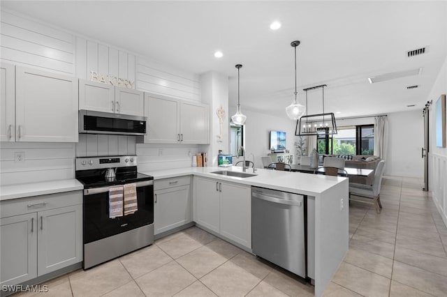 kitchen with stainless steel appliances, kitchen peninsula, light tile patterned floors, sink, and decorative light fixtures