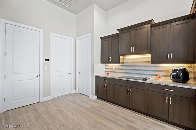 kitchen featuring black electric stovetop, decorative backsplash, light wood-type flooring, dark brown cabinets, and light stone counters