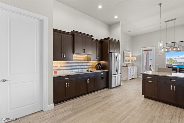 kitchen featuring decorative light fixtures, light hardwood / wood-style floors, dark brown cabinetry, and stainless steel refrigerator