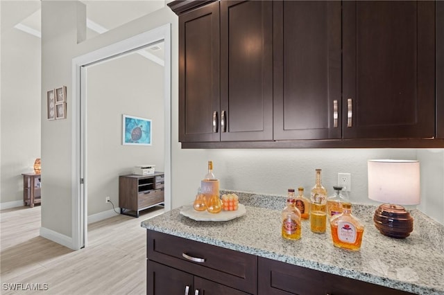 kitchen with dark brown cabinets, light stone counters, and light hardwood / wood-style flooring