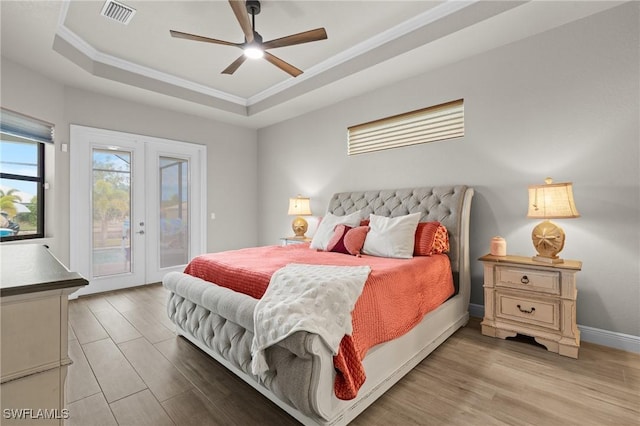 bedroom with french doors, access to outside, light wood-type flooring, ceiling fan, and a tray ceiling