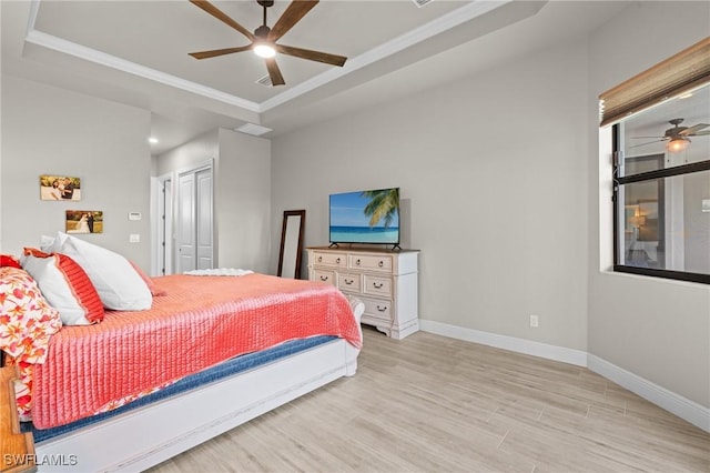 bedroom featuring ceiling fan, a tray ceiling, light hardwood / wood-style flooring, ornamental molding, and a closet