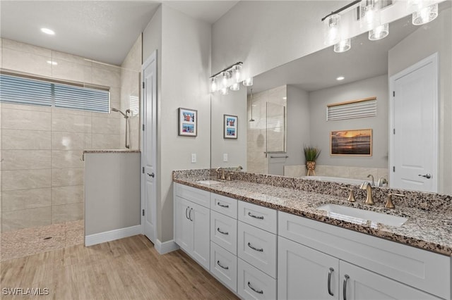 bathroom with hardwood / wood-style floors, tiled shower, and vanity