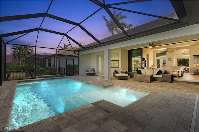 pool at dusk with an outdoor hangout area, glass enclosure, a patio area, and a ceiling fan