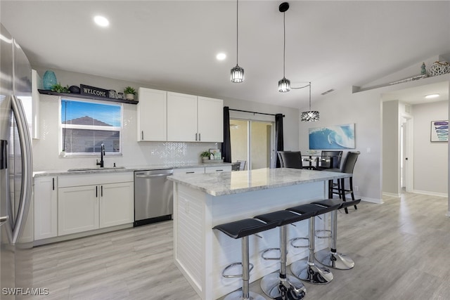 kitchen with appliances with stainless steel finishes, light stone counters, white cabinets, lofted ceiling, and sink