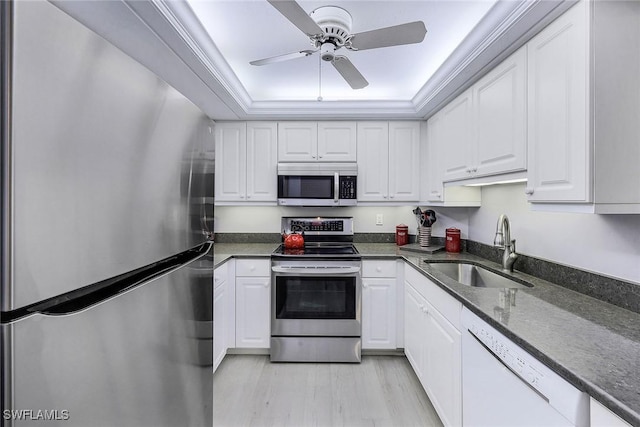 kitchen featuring stainless steel appliances, a raised ceiling, white cabinets, dark stone countertops, and sink