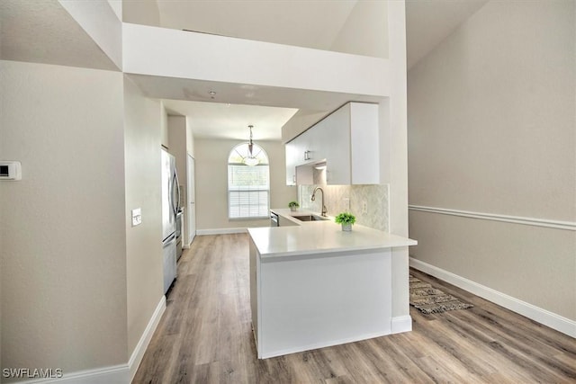 kitchen featuring white cabinets, sink, hanging light fixtures, kitchen peninsula, and light wood-type flooring