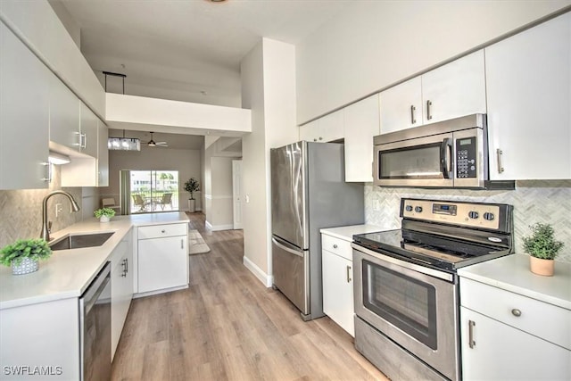 kitchen featuring appliances with stainless steel finishes, a towering ceiling, white cabinetry, sink, and ceiling fan