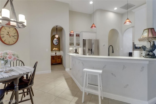 kitchen featuring pendant lighting, a towering ceiling, white cabinetry, stainless steel fridge with ice dispenser, and light tile patterned floors