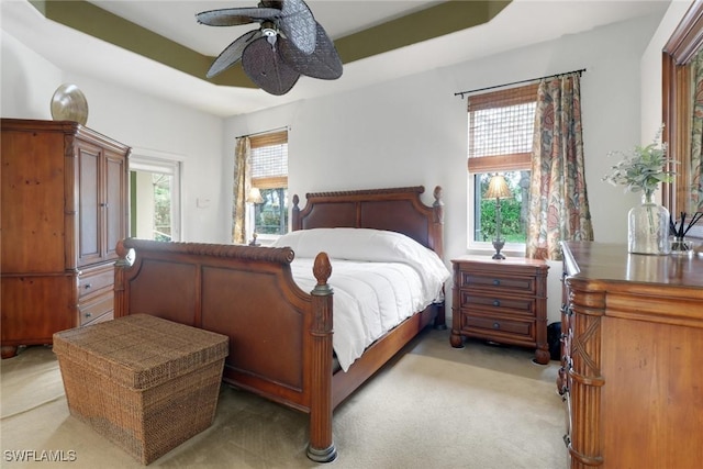 bedroom with ceiling fan, light carpet, and a raised ceiling