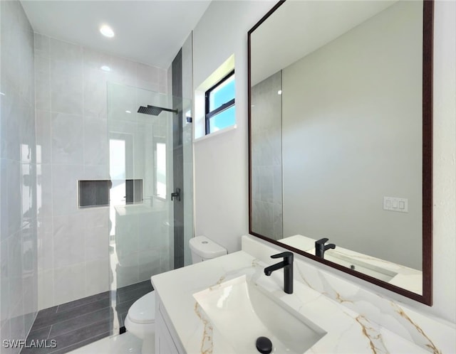 bathroom featuring a tile shower, vanity, and toilet