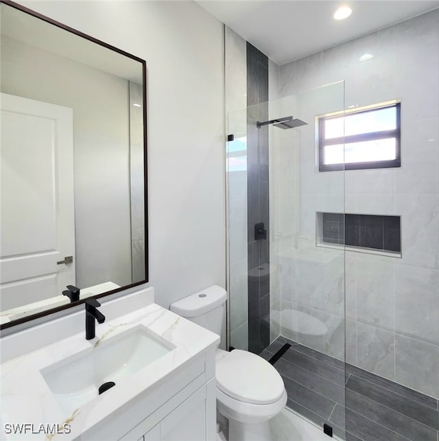 bathroom with toilet, a tile shower, and vanity