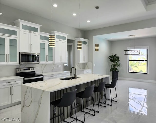 kitchen featuring light stone counters, stainless steel appliances, a center island with sink, white cabinets, and sink