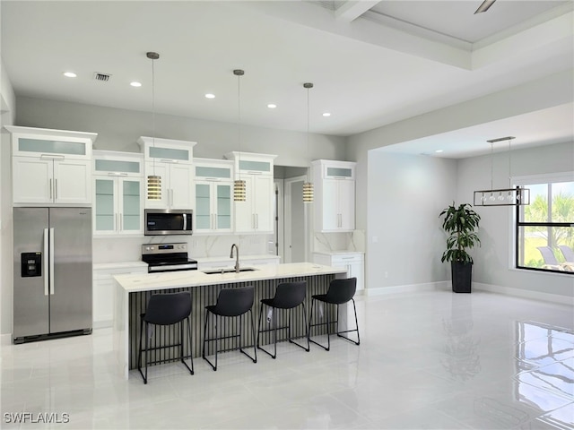 kitchen with appliances with stainless steel finishes, hanging light fixtures, white cabinetry, and a center island with sink