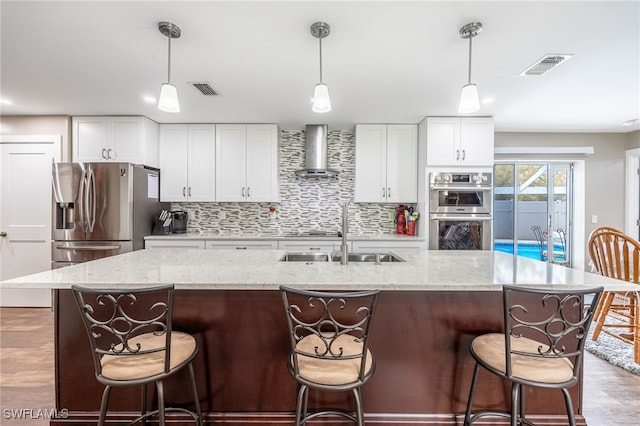 kitchen featuring decorative light fixtures, white cabinets, wall chimney exhaust hood, and stainless steel appliances