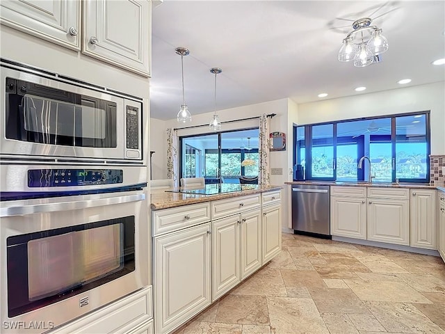 kitchen with decorative light fixtures, sink, white cabinets, light stone counters, and stainless steel appliances