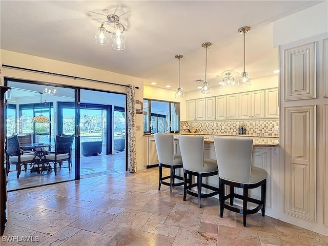 kitchen featuring a kitchen bar, a center island, hanging light fixtures, light stone countertops, and decorative backsplash