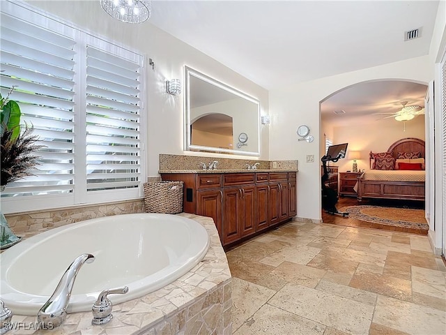 bathroom with a relaxing tiled tub, ceiling fan, and vanity