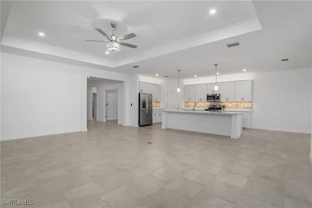 unfurnished living room with visible vents, baseboards, a ceiling fan, a tray ceiling, and a sink