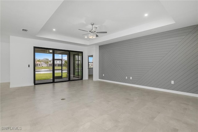 spare room with a raised ceiling, visible vents, ceiling fan, and baseboards