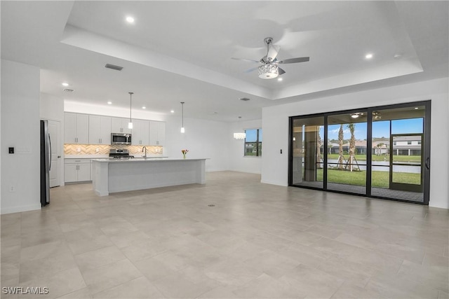 unfurnished living room featuring a tray ceiling, a healthy amount of sunlight, and visible vents