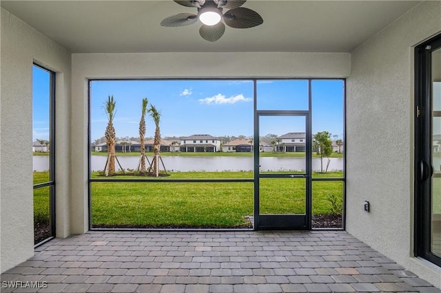 unfurnished sunroom with ceiling fan, a water view, and a residential view