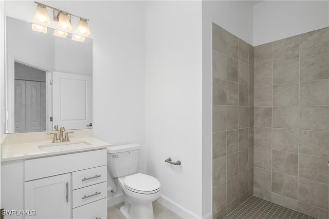 bathroom with toilet, vanity, baseboards, a closet, and a tile shower