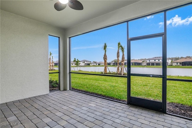 unfurnished sunroom with a residential view, a water view, and ceiling fan