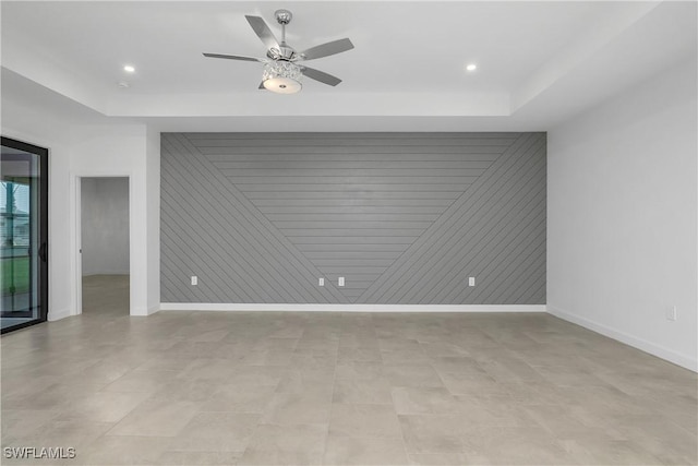 unfurnished room featuring an accent wall, a raised ceiling, and baseboards