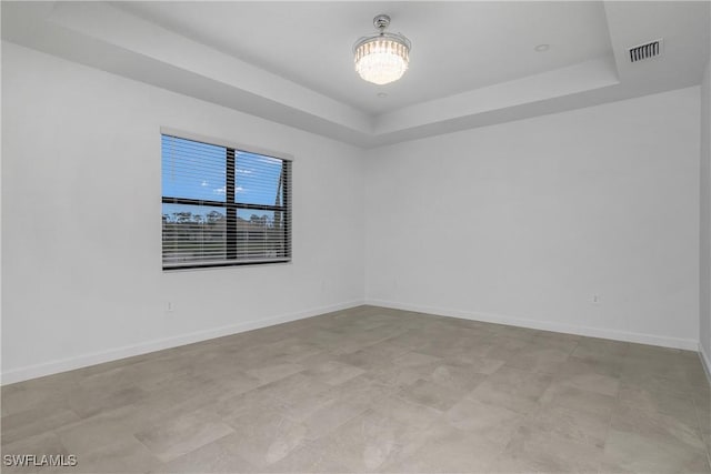 empty room with a raised ceiling, visible vents, and baseboards