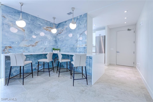 kitchen with kitchen peninsula, hanging light fixtures, white cabinetry, stainless steel refrigerator, and a kitchen breakfast bar