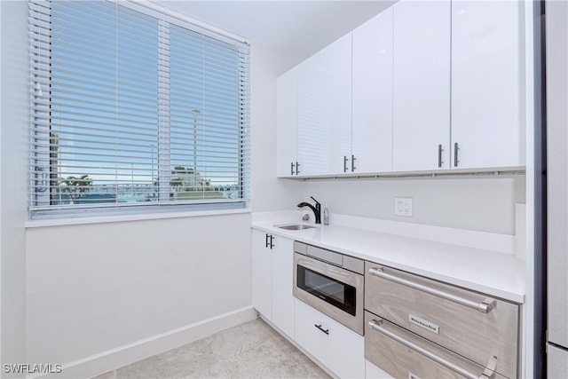 kitchen featuring sink, stainless steel microwave, and white cabinetry