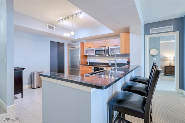 kitchen featuring kitchen peninsula, hanging light fixtures, light brown cabinetry, a breakfast bar area, and appliances with stainless steel finishes