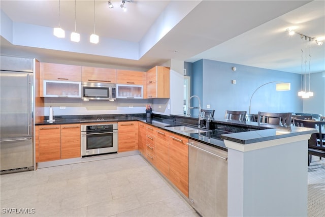 kitchen featuring appliances with stainless steel finishes, kitchen peninsula, dark stone counters, pendant lighting, and sink