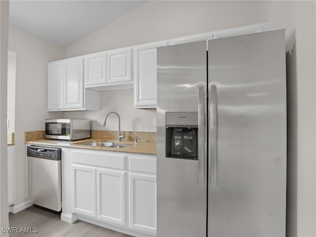 kitchen featuring appliances with stainless steel finishes, white cabinetry, sink, vaulted ceiling, and light stone counters