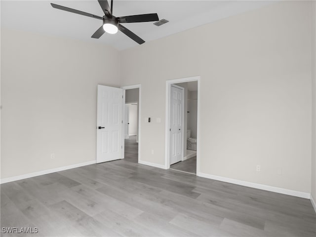 unfurnished bedroom with ceiling fan, a high ceiling, hardwood / wood-style flooring, and ensuite bath