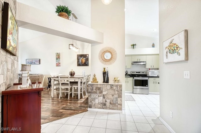 kitchen with stainless steel electric range, high vaulted ceiling, and light tile patterned floors