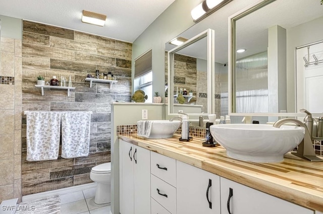 bathroom featuring tile patterned flooring, toilet, vanity, tile walls, and a textured ceiling