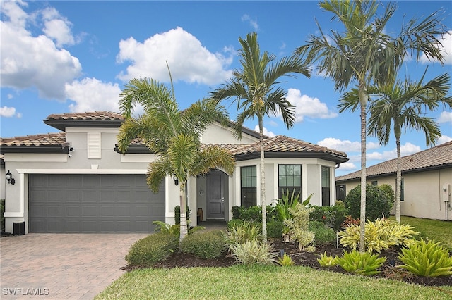 mediterranean / spanish-style home with a tile roof, decorative driveway, a garage, and stucco siding