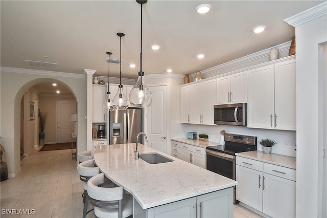 kitchen featuring a kitchen island with sink, a sink, arched walkways, appliances with stainless steel finishes, and white cabinets