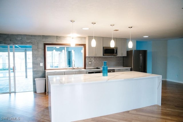 kitchen featuring sink, appliances with stainless steel finishes, hanging light fixtures, a center island, and light stone countertops