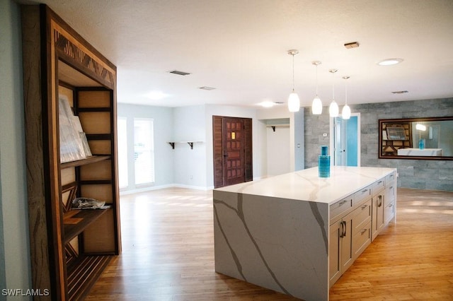 kitchen with light stone counters, tile walls, light wood-type flooring, a kitchen island, and pendant lighting