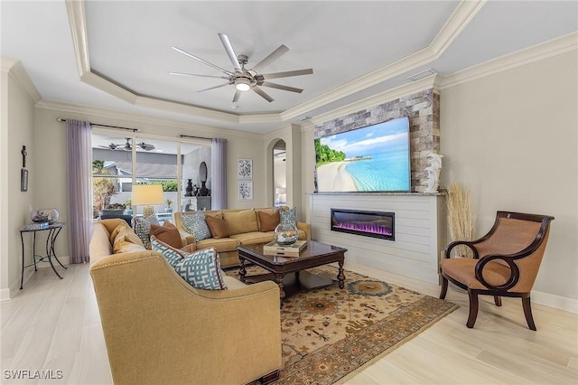 living room featuring ceiling fan, a fireplace, crown molding, and a tray ceiling